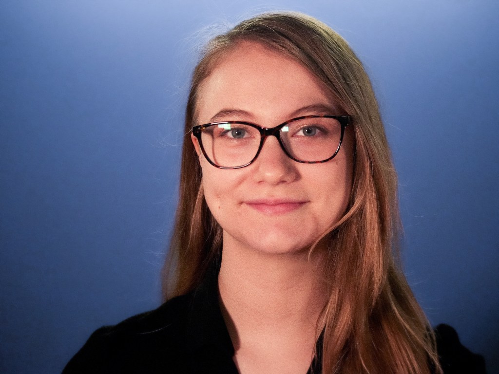 Kara looking into the camera, wearing glasses and a black shirt.